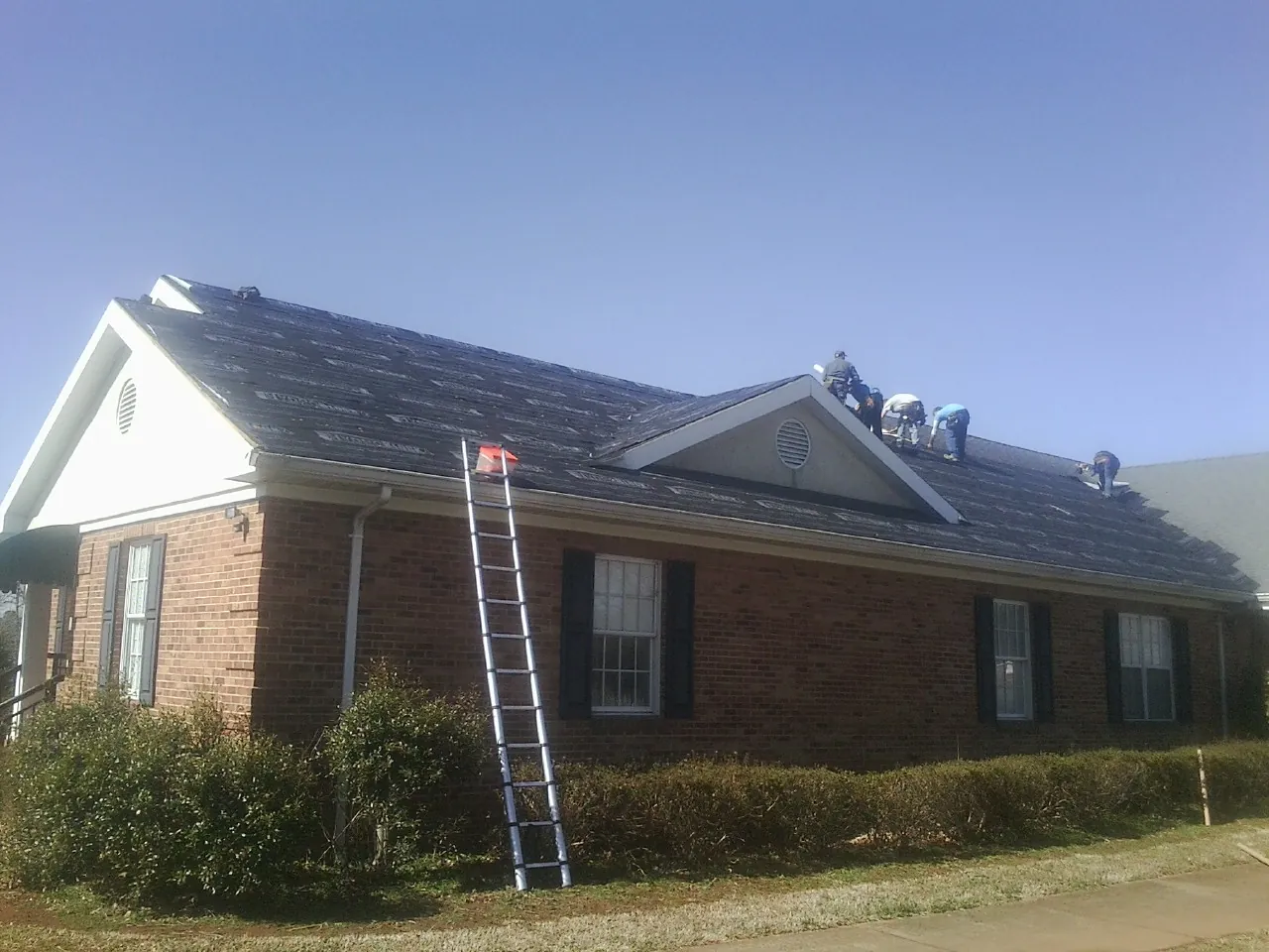 Crew tearing shingles off a brick ranch roof with a ladder set — Metal Roof Repair work by our crew in South Hamilton