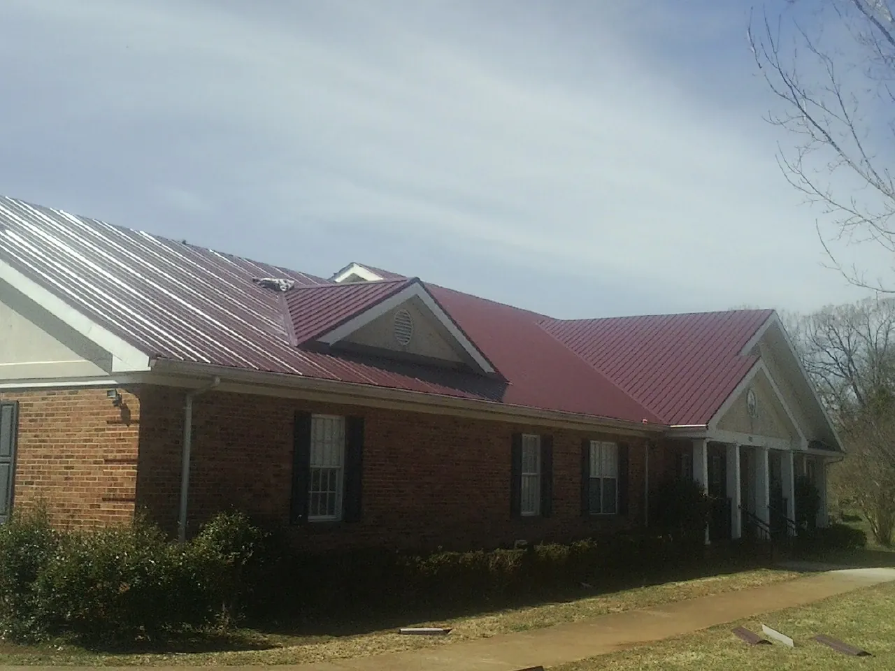Red metal roof with gabled entries on a long brick building, from a Hail Damage Roof Repair job in South Hamilton