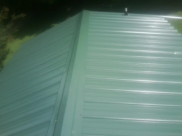New green metal panels meeting at the ridge of a roof — Flat Roof Repair work by our crew in South Hamilton