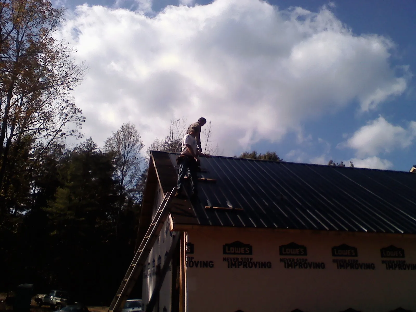 Roofer fastening dark metal panels high against a cloudy sky, from a Roof Inspection job in South Hamilton