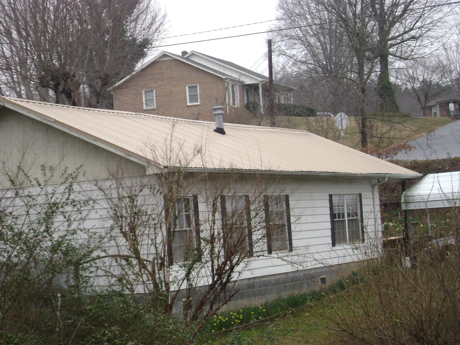 Tan metal roof on a white sided house set into a hillside — Commercial Roofing by Roofing Brothers in South Hamilton