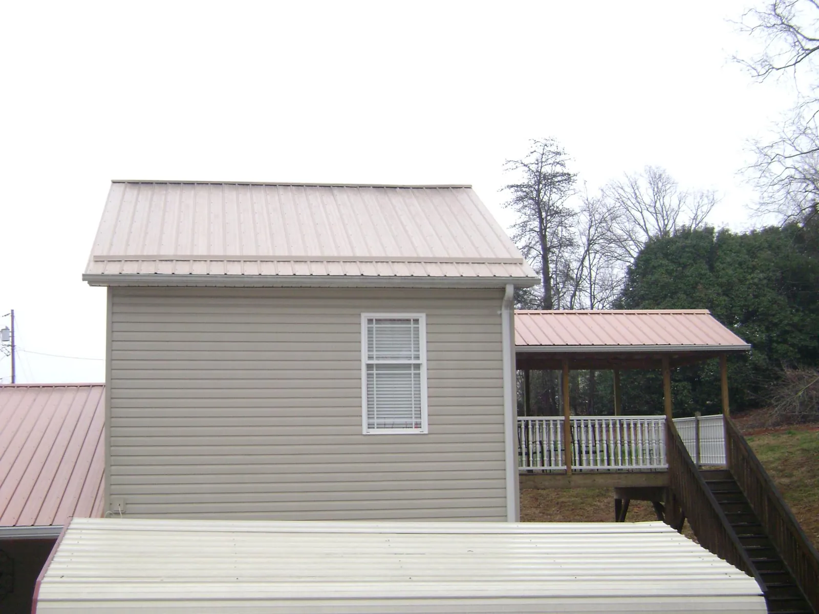 Tan metal roofs on a two story addition and attached porch, from a Roof Replacement job in South Hamilton